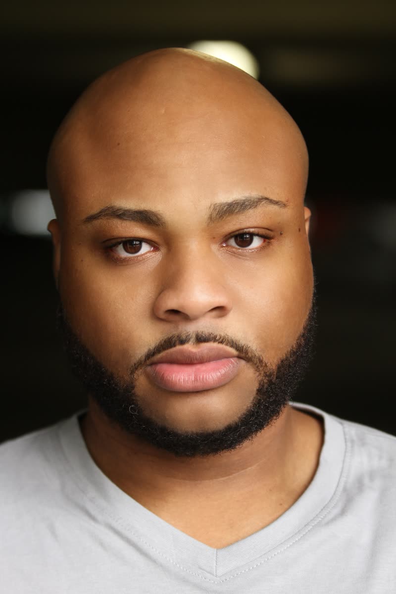 Close-up theatrical headshot of Scottie Stowe in a grey v-neck